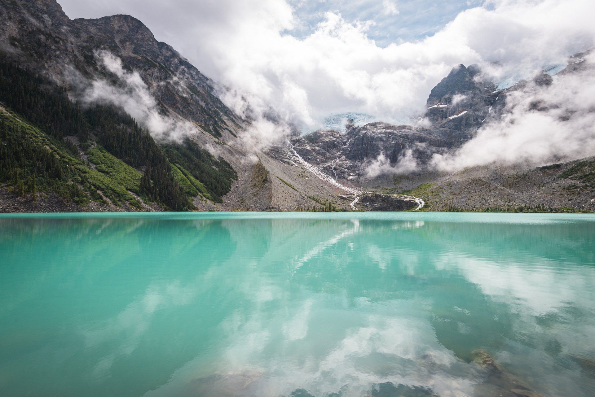 Upper Joffre lake with surrounding mountains and glacier behind the low clouds, Joffre Lakes Provincial Park, BC, Canada