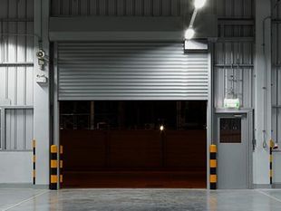 Muelle de carga del almacén con puerta enrollable gris parcialmente abierta, salida de emergencia.