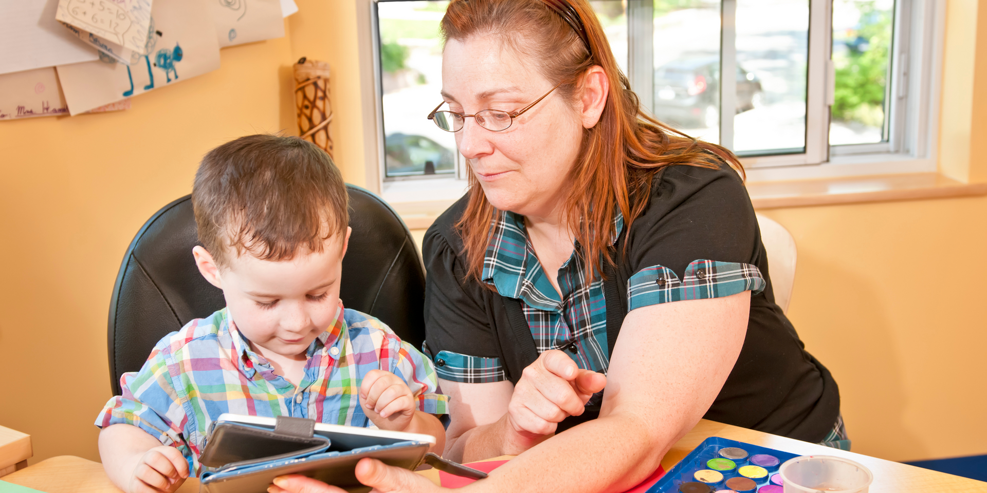 A woman is teaching a young boy how to use a tablet computer.