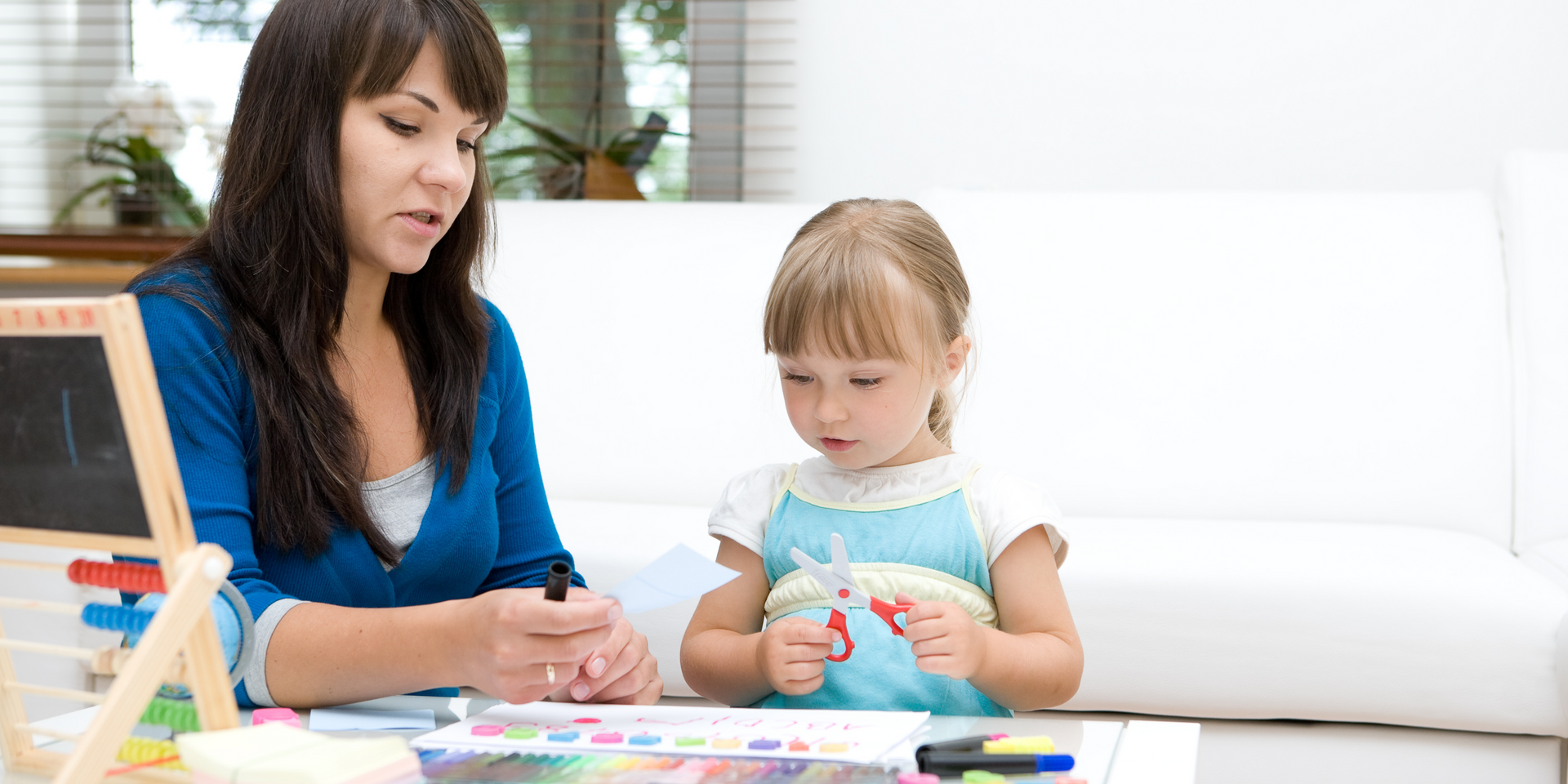 A woman is teaching a little girl how to use scissors.