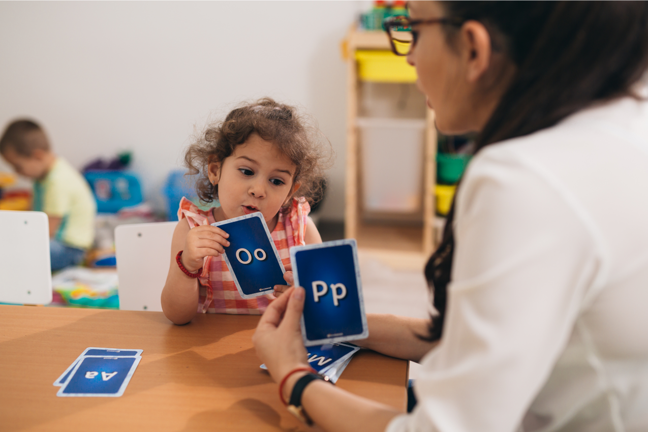A woman is teaching a little girl how to read the letters of the alphabet.