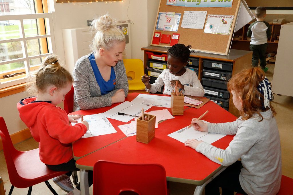 A group of children are sitting at a table with a teacher.