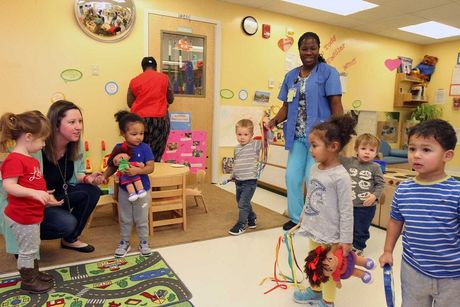 A group of children are playing in a room with a nurse.