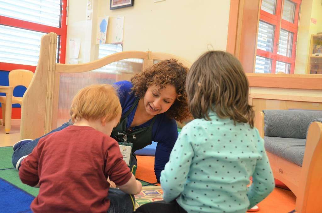 A woman is reading a book to two children in a classroom.