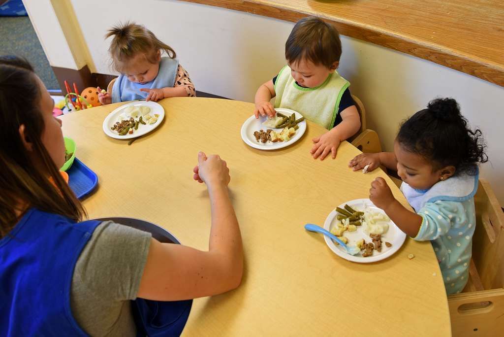 A woman is sitting at a table with three children eating food.
