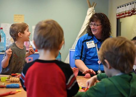 A woman in a blue shirt is talking to a group of children.