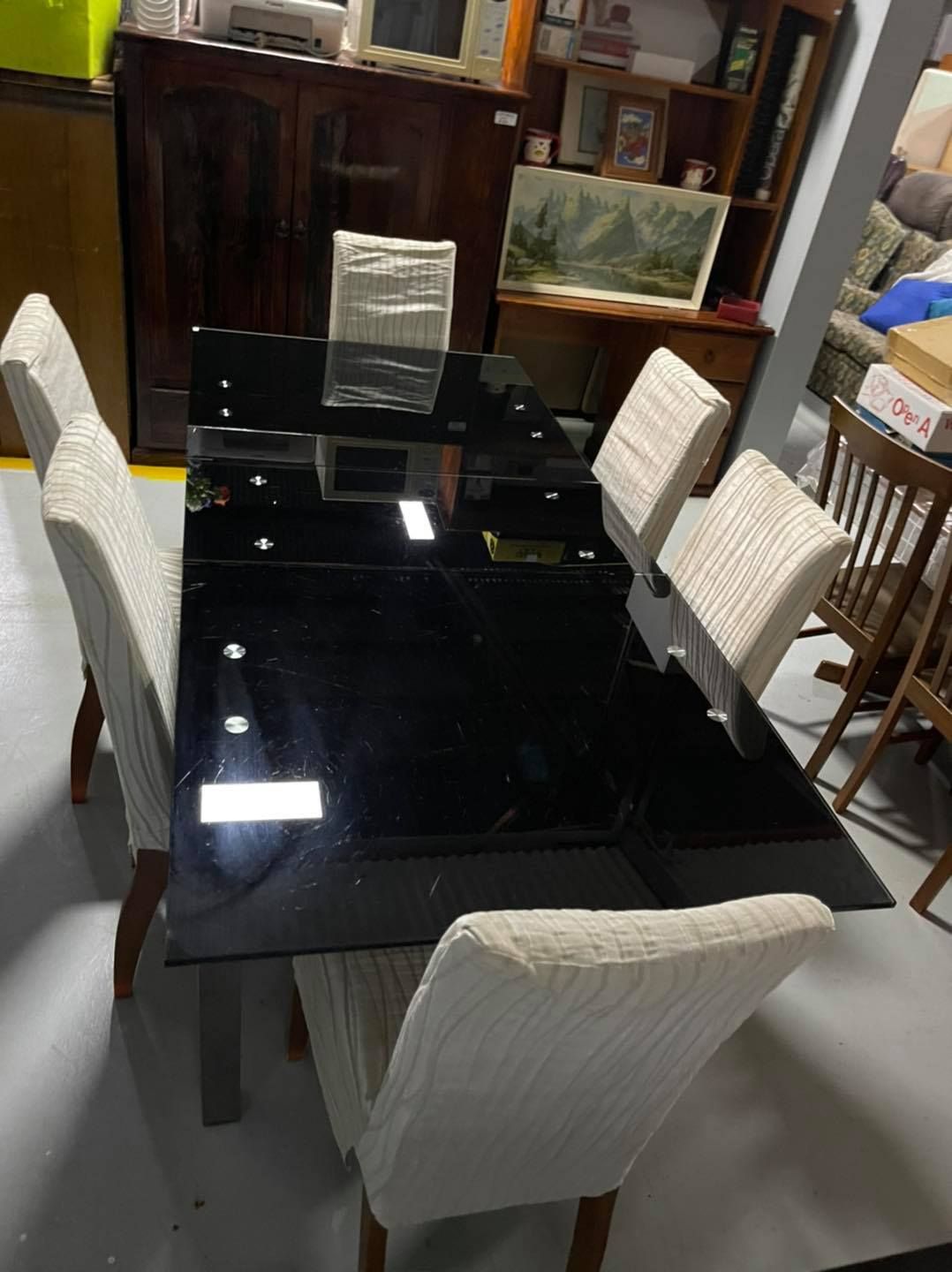 A Black Glass Dining Table With White Chairs In A Room — Anton's New & Used Furniture In Ciccone, NT