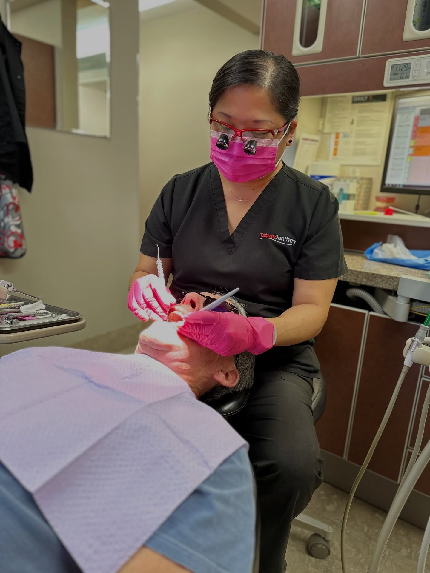 Dentist treating patient in a pink mask in a dental exam room