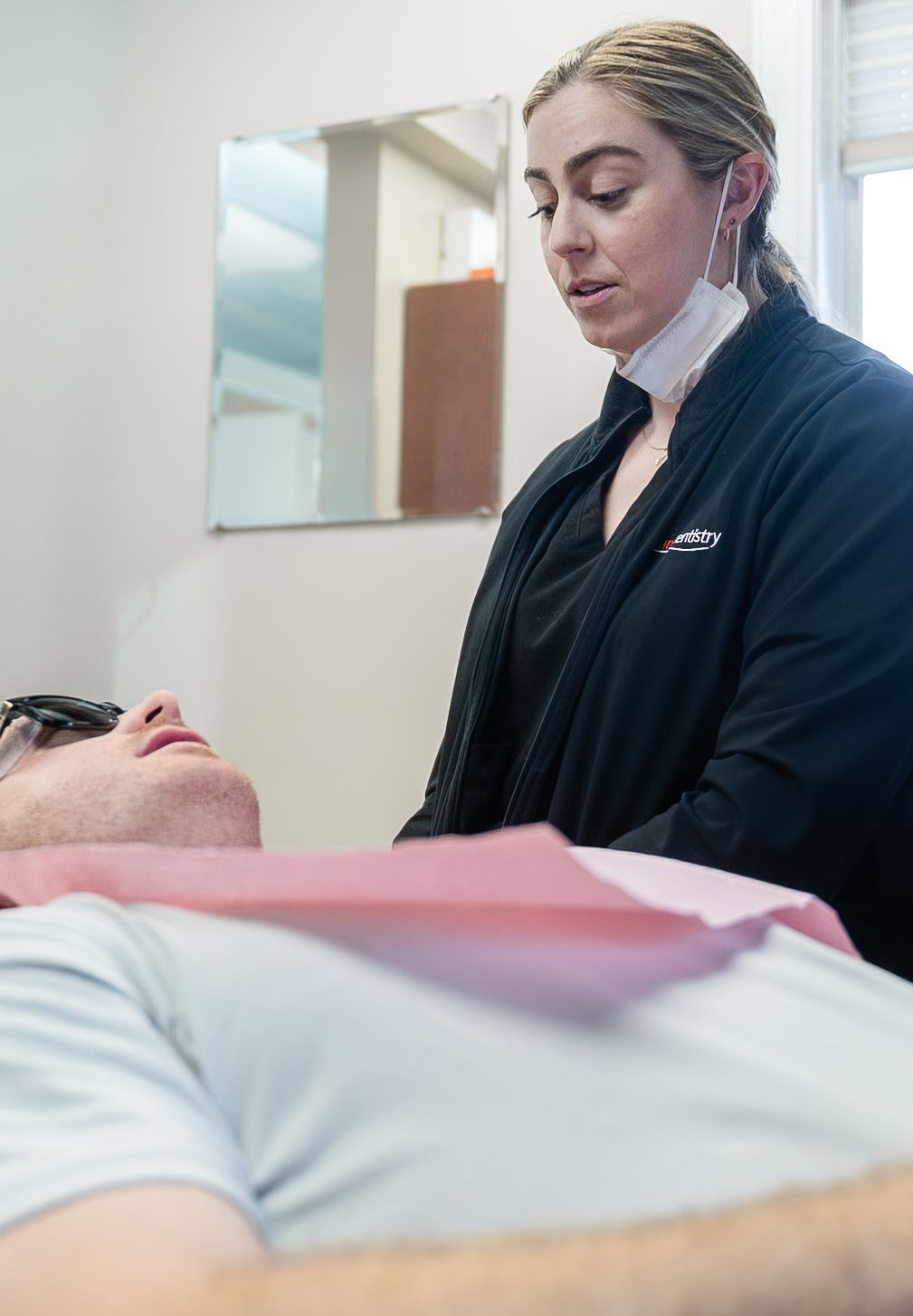 Dentist examining a patient in a clinic, with a dental bib and a mirror on the wall