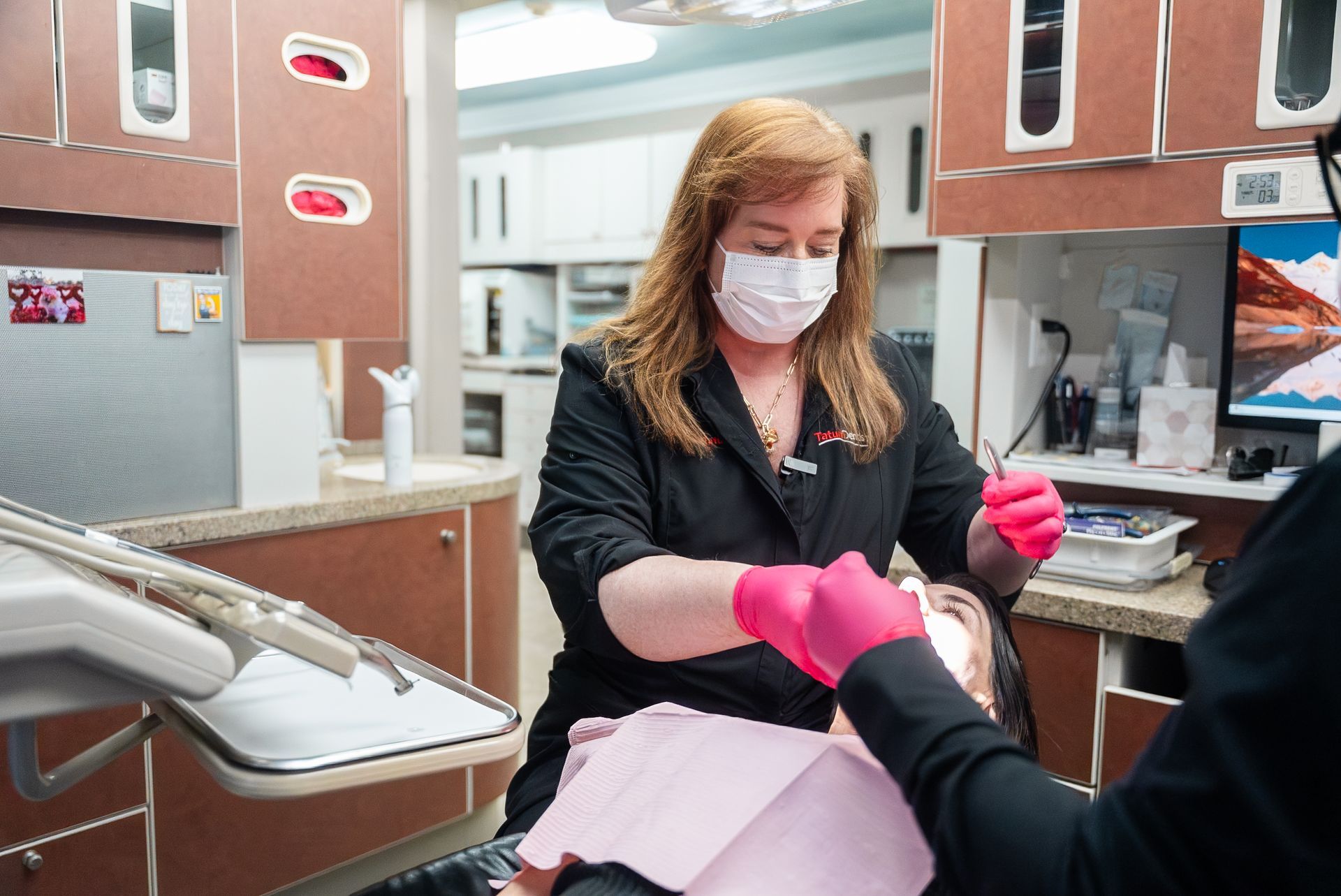 Dental hygienist in mask and pink gloves cleaning a patient’s mouth in a clinic chair