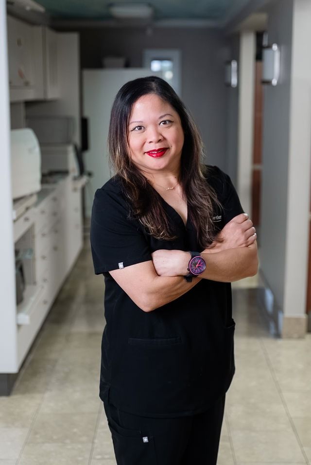 Woman in black scrubs standing with arms crossed in a hallway