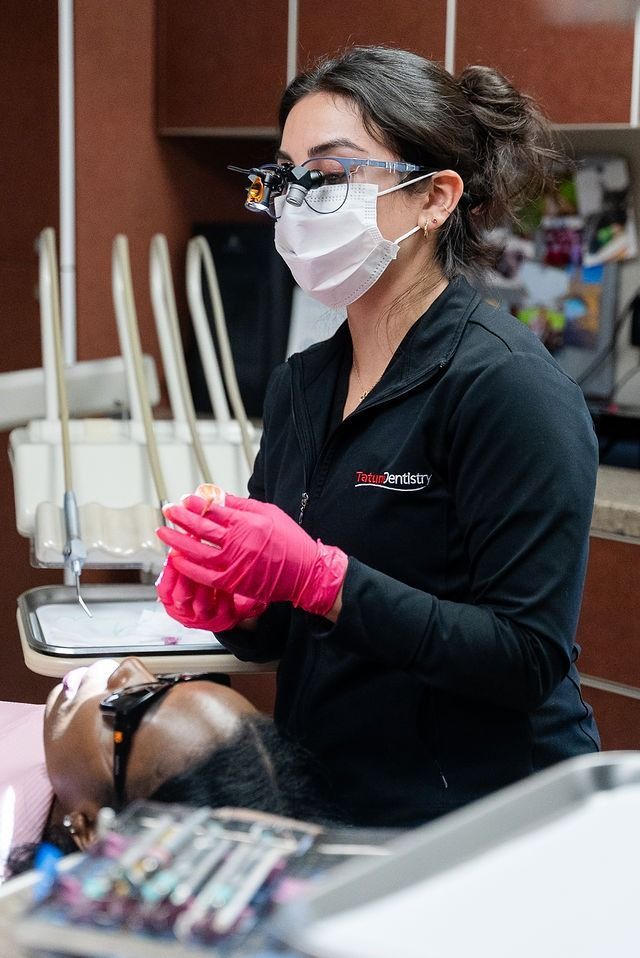 Dentist wearing a mask and pink gloves working in a clinic chair area
