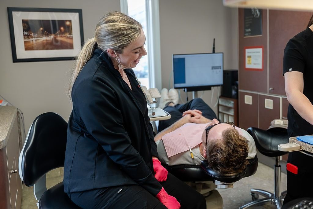 Person in black coat leans over a dental patient reclined in a chair