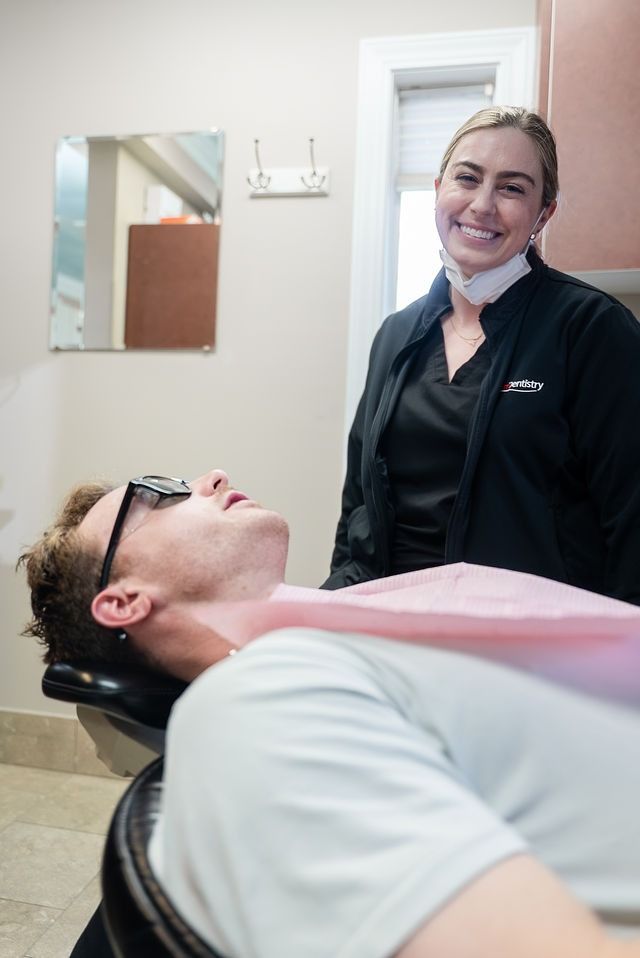 Dentist smiling beside a reclined patient in a dental exam room