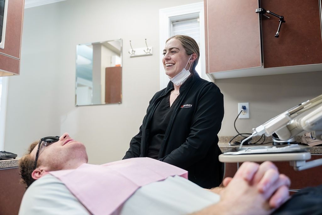 Dentist smiling beside a reclining patient in a dental exam room