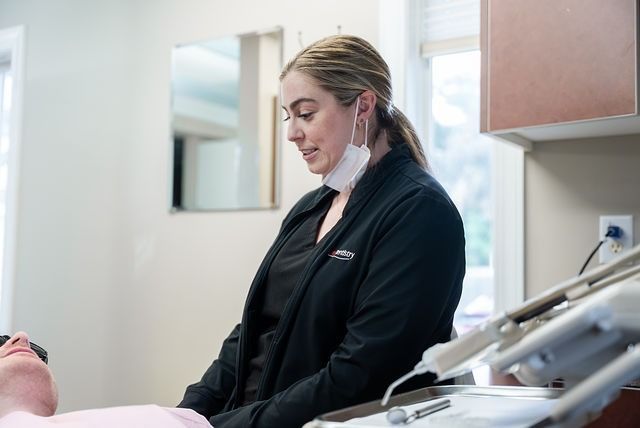 Dental professional standing beside a reclining patient in a bright clinic room