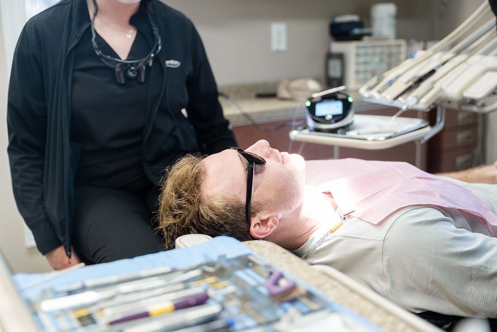 Person reclines in dental chair while clinician stands nearby
