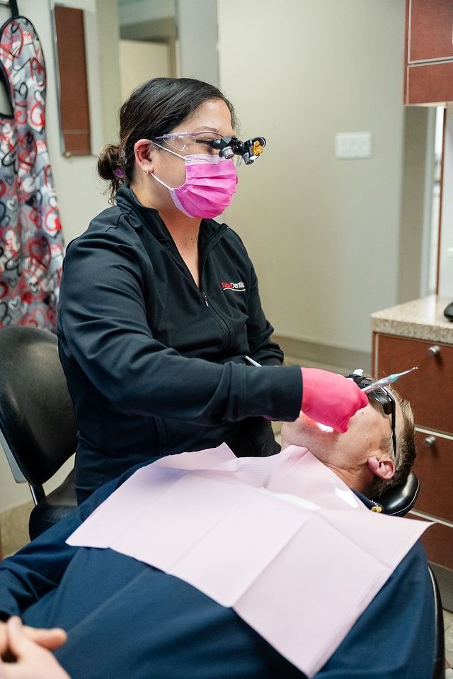 Dentist in black attire and pink mask examines a patient