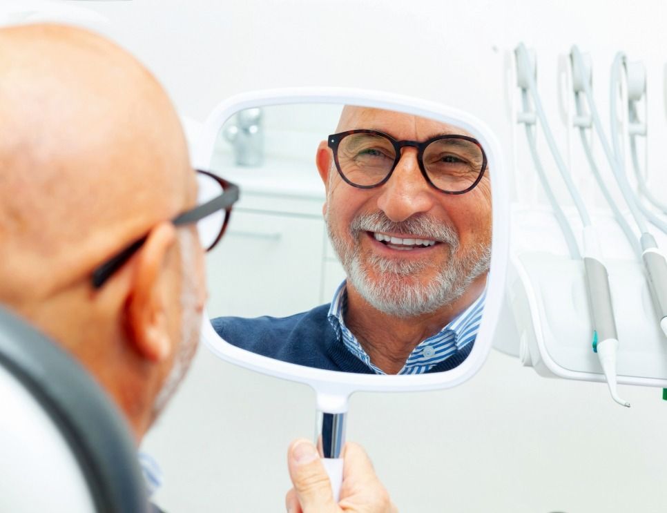 Man smiling at dental mirror in a bright clinic, with dental tools visible nearby