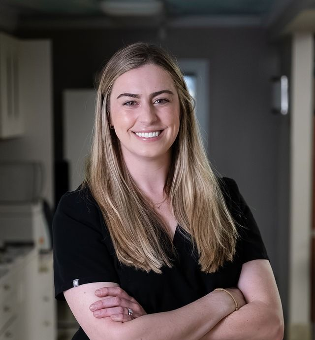 Smiling woman in a black shirt standing with arms crossed in a hallway