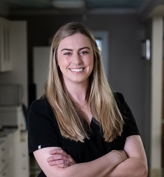 Smiling woman in a black shirt standing with arms crossed in a hallway