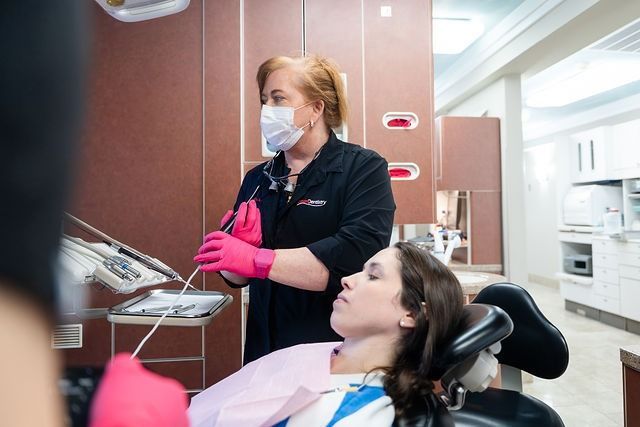 Dental hygienist wearing pink gloves works beside a reclining patient