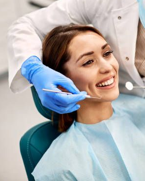 Dentist wearing blue gloves examining a smiling patient in a dental chair