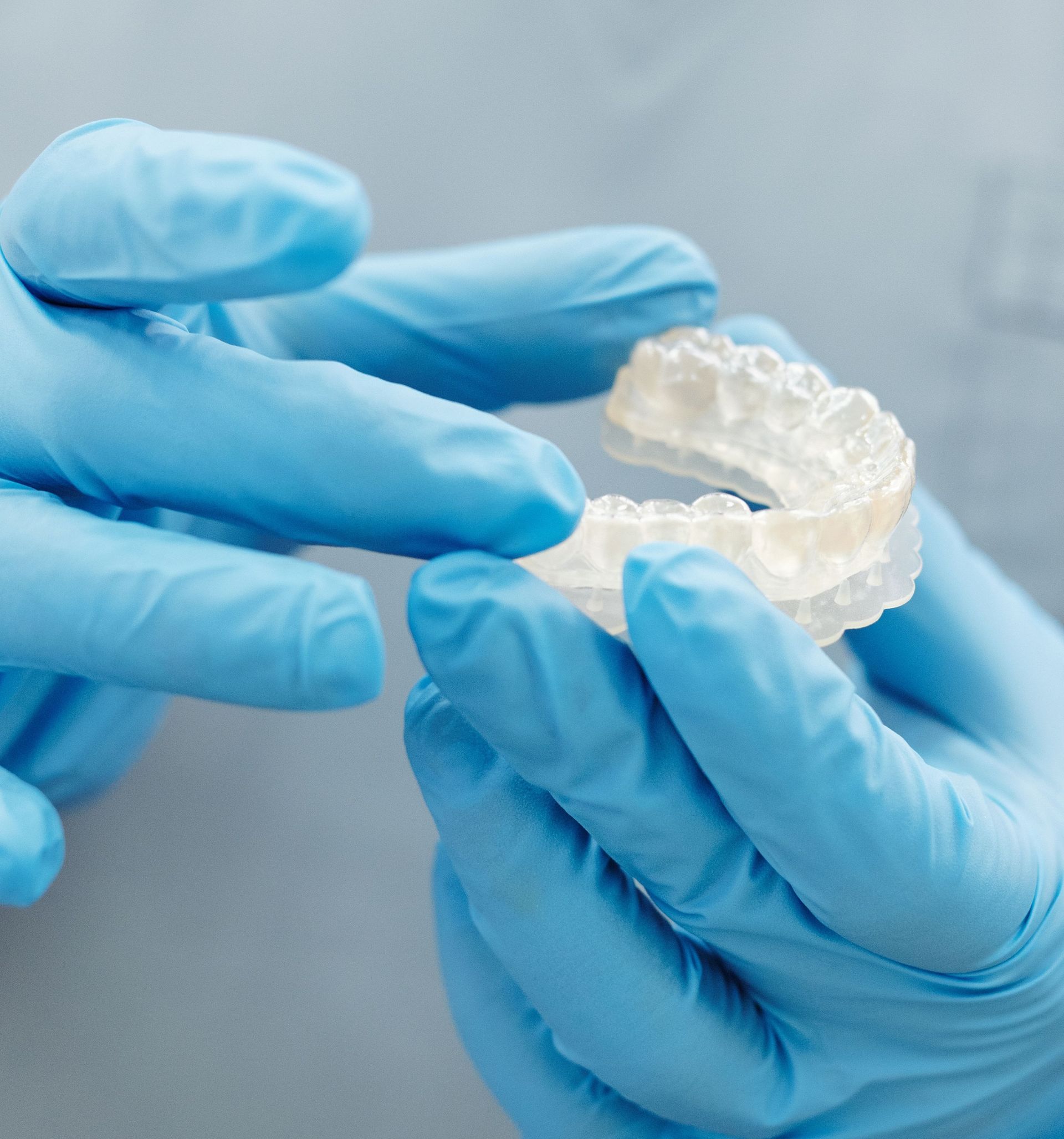 Gloved hands holding a clear dental aligner against a gray background