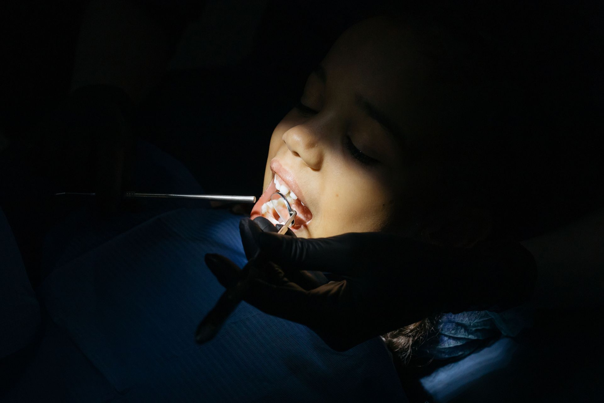 Person reclining in a dark dental chair during a dental procedure