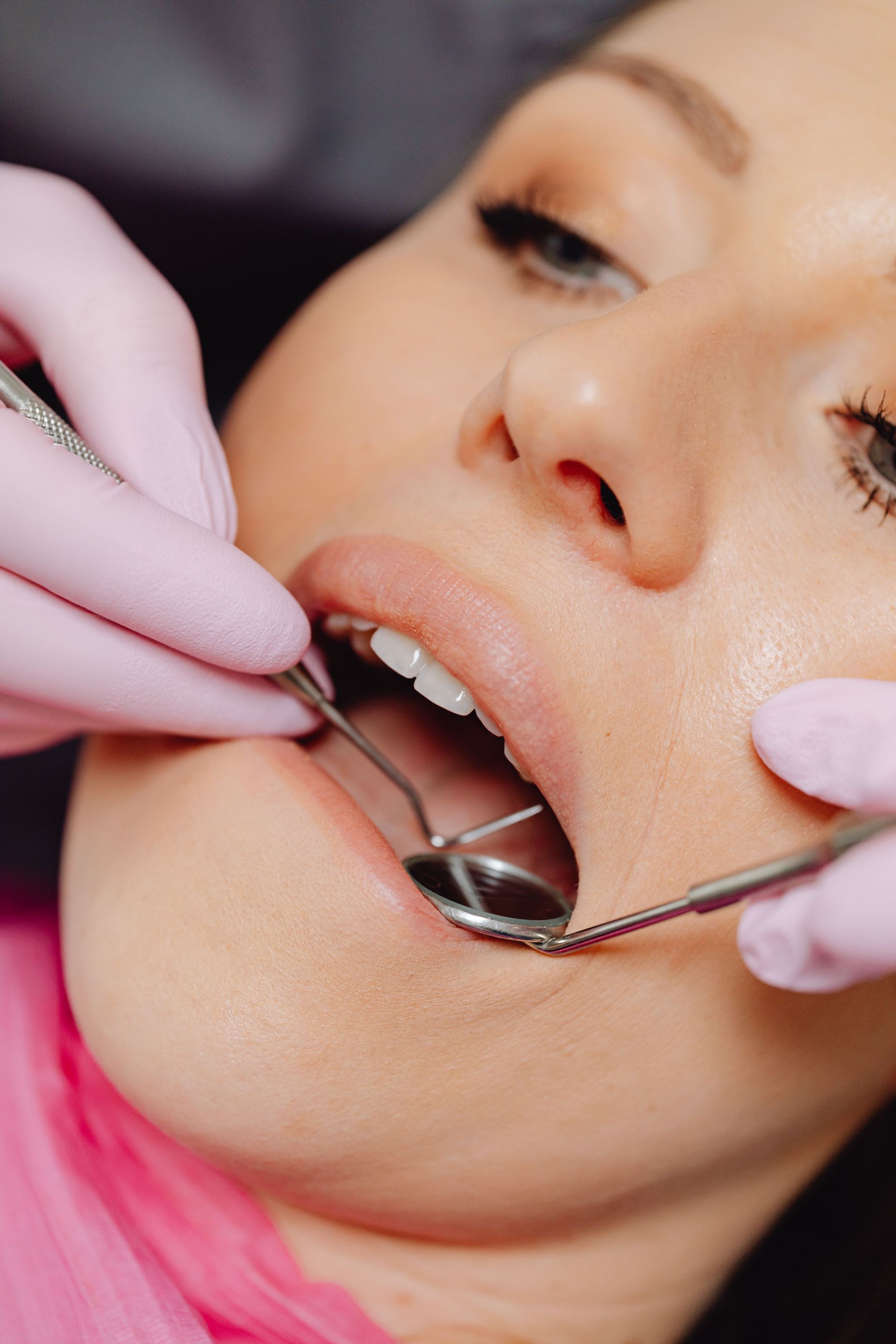 Dentist using a dental mirror and tools to examine a patient’s open mouth