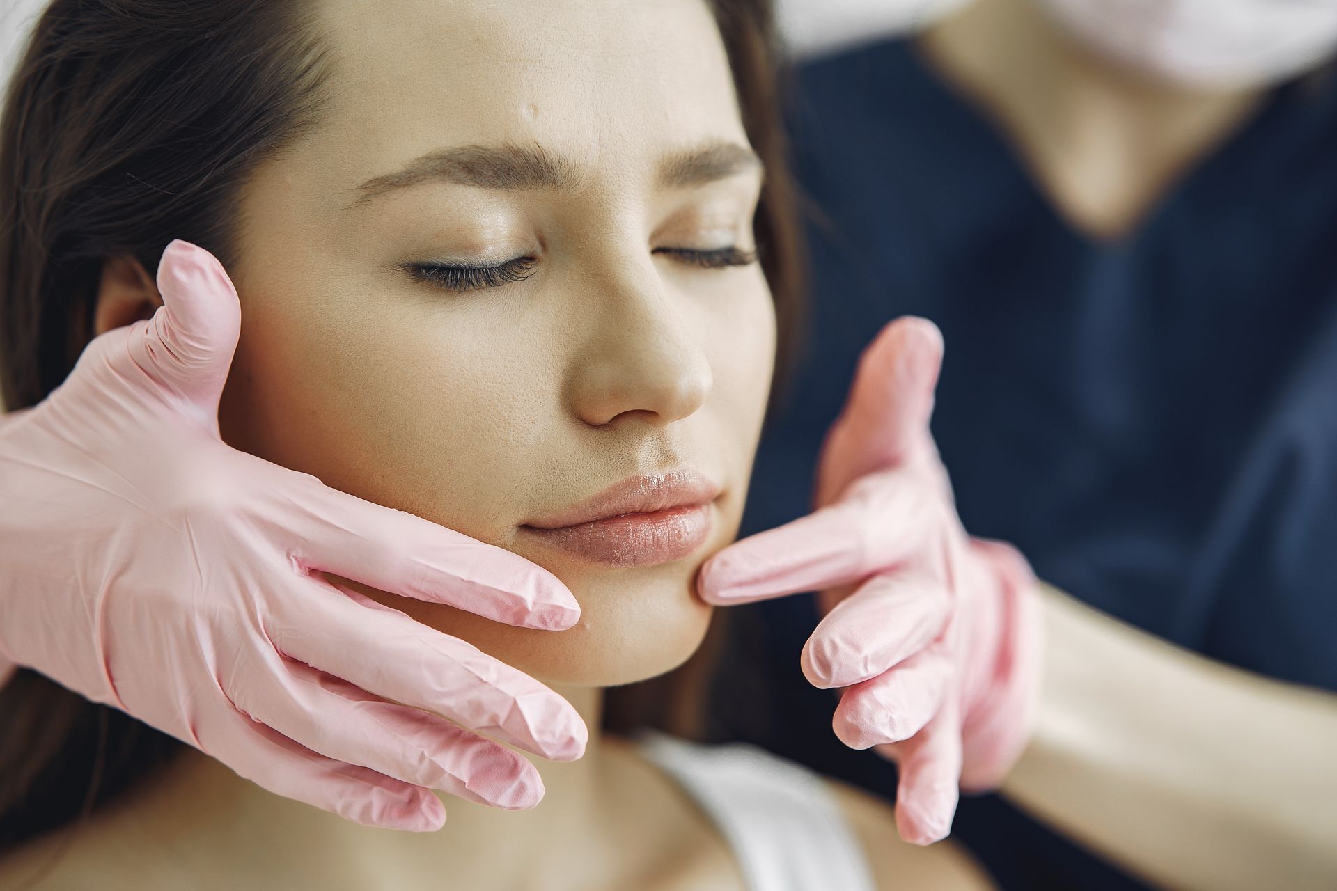 Gloved hands gently adjust a woman’s face during a cosmetic treatment