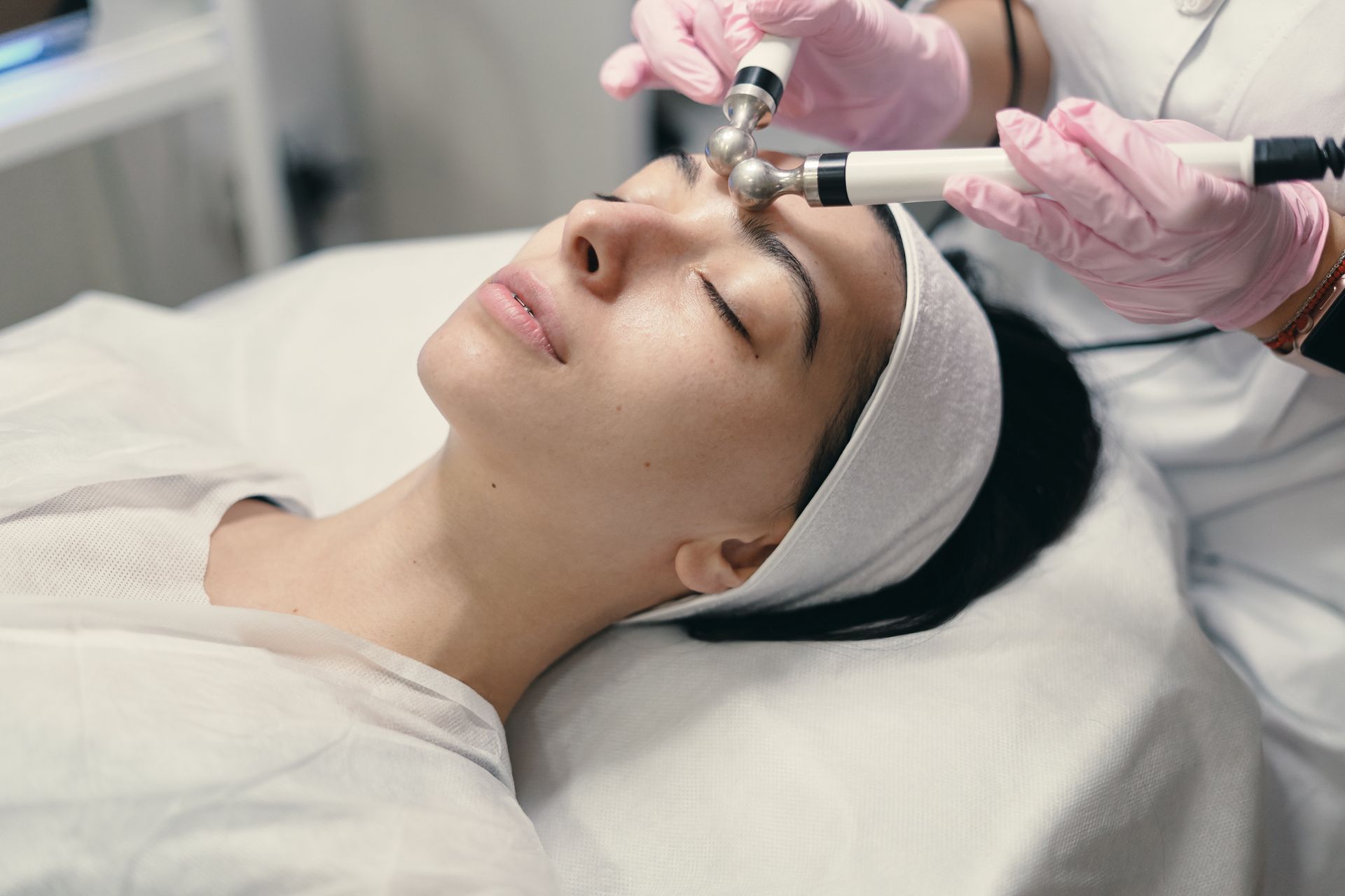 A woman relaxing during a facial treatment, with a warm towel wrapped around her hair.
