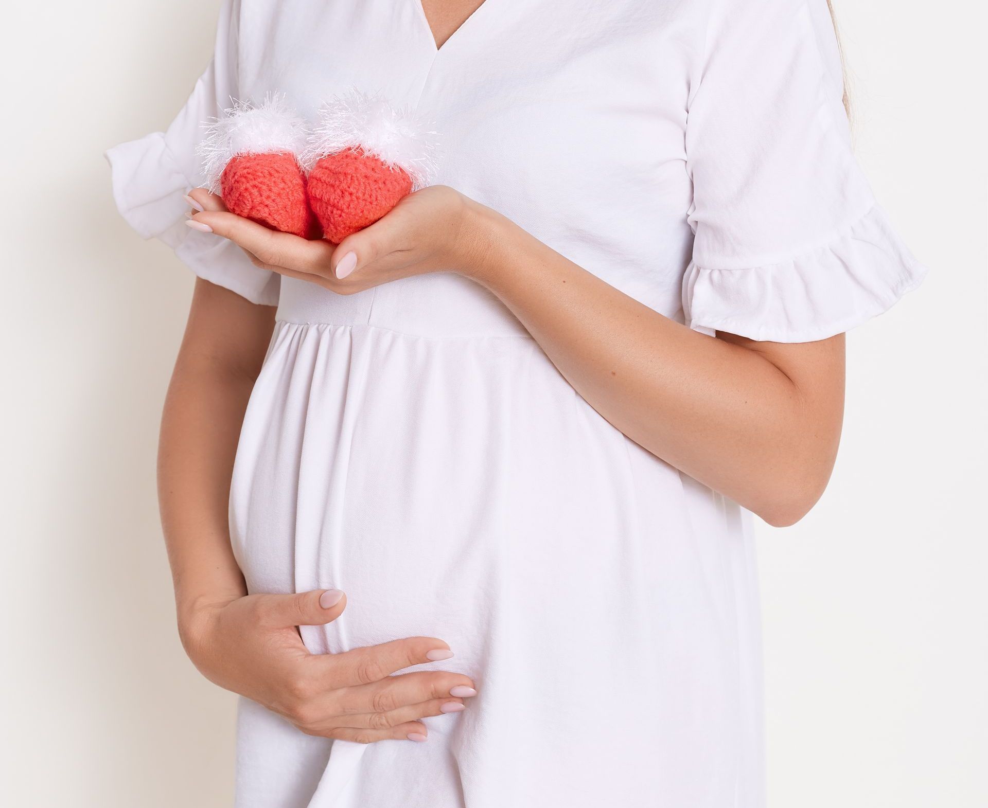 A pregnant woman holding baby shoes while gently cradling her belly, symbolizing the safe and soothing Exfoliating Pregnancy Facial at Devine Medspa for moms-to-be.