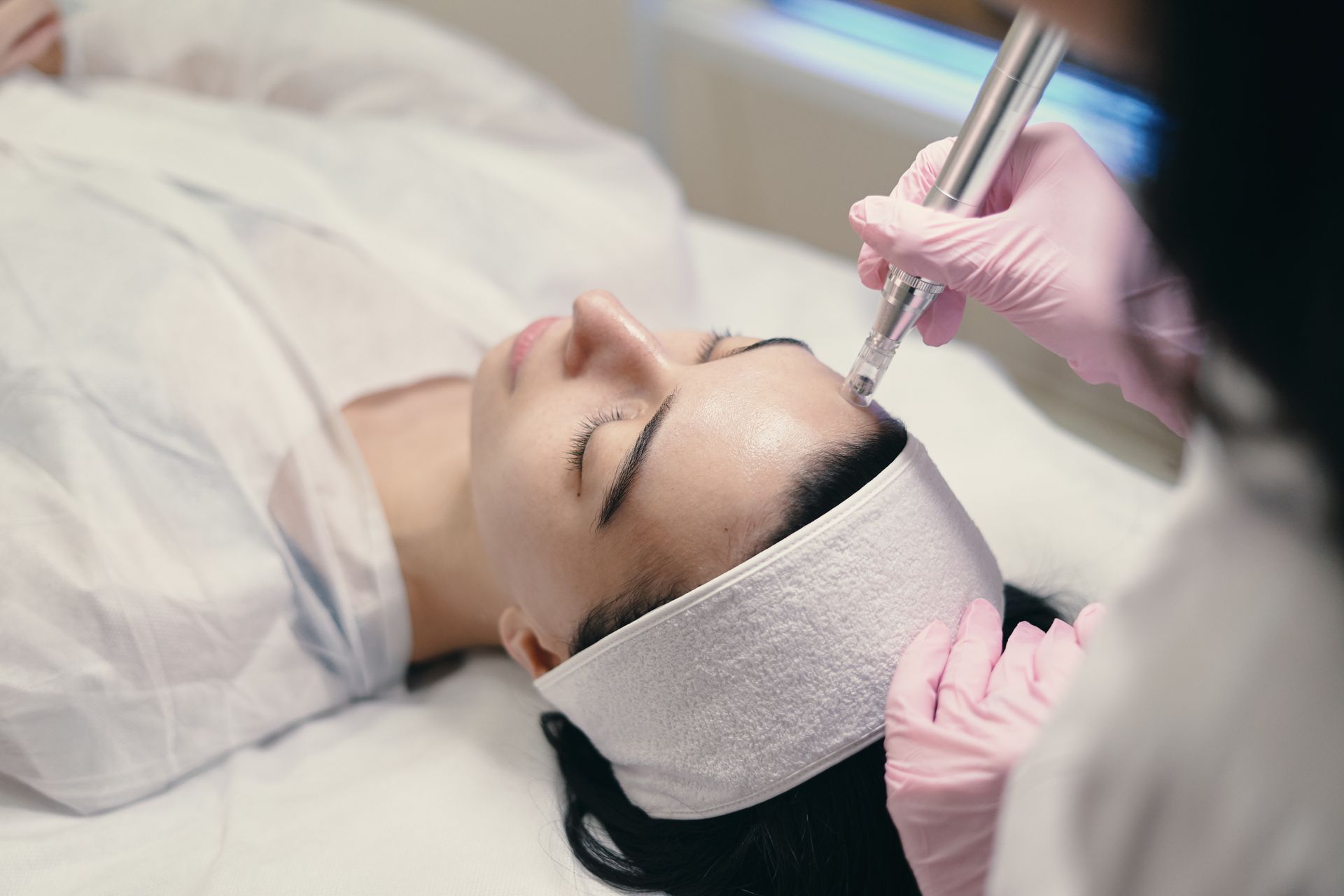 A woman relaxing during a facial treatment, with a warm towel wrapped around her hair.