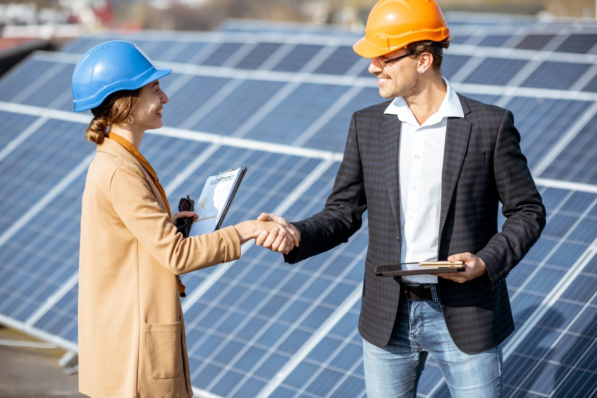 Ein Mann und eine Frau schütteln vor Solarmodulen die Hände.