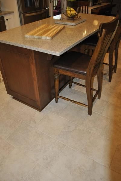 Kitchen island with a light-colored countertop, dark wood cabinets, and two wooden bar stools.