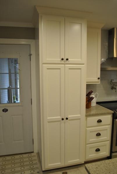 Tall white kitchen cabinet next to a door, with lower drawers and countertop.