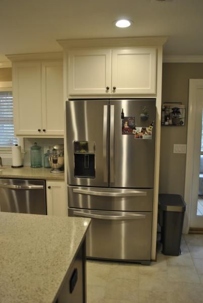 Stainless steel refrigerator in kitchen with white cabinets.