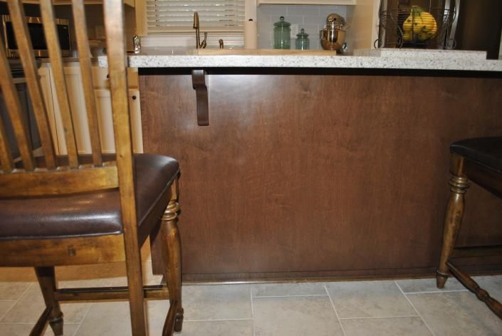 Brown wooden kitchen island with a granite countertop, with a chair on either side, facing it.