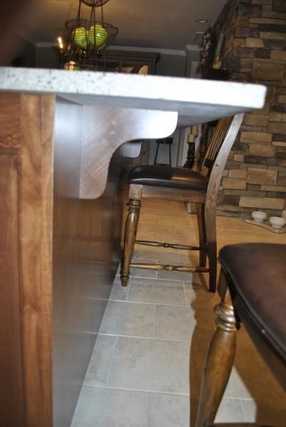 A kitchen countertop with a curved support; two wooden chairs sit in front of it.