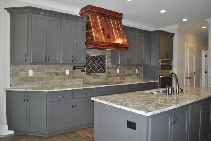 Gray kitchen with a wooden range hood, granite countertops, and an island.