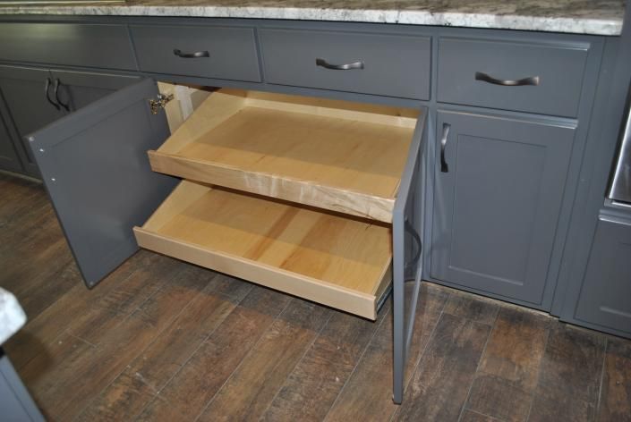 Gray kitchen cabinet with pull-out shelves, open. Wooden shelves in a gray cabinet on brown floor.