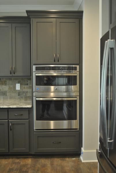 Dark gray kitchen cabinets with a built-in double oven and a stainless steel refrigerator.
