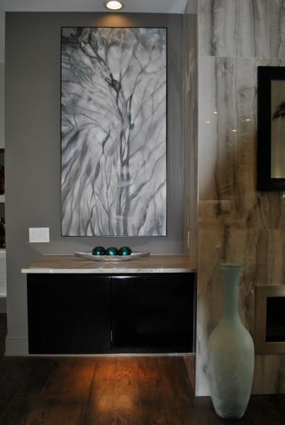 Black cabinet below a tall gray and white artwork, topped with a bowl and orbs. A vase stands to the right.