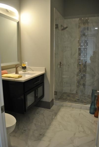Bathroom with dark vanity, white countertop, marble floor, and glass shower.