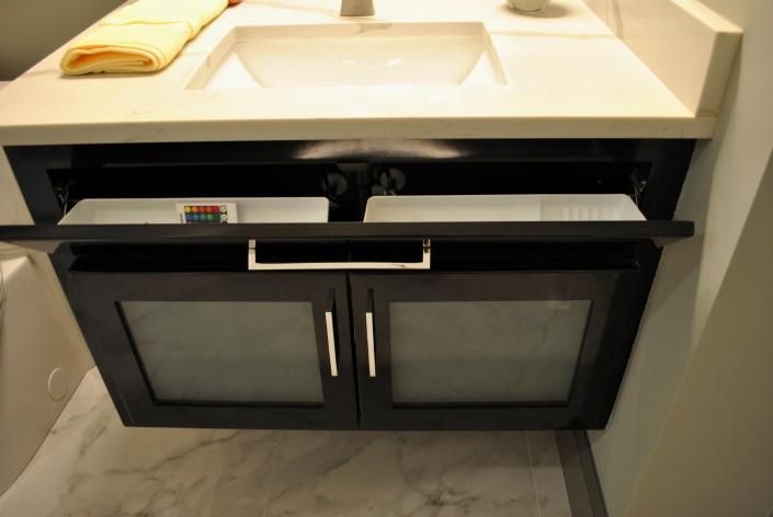 Bathroom vanity with open cabinet doors revealing two pull-out trays and lower glass-paneled doors.