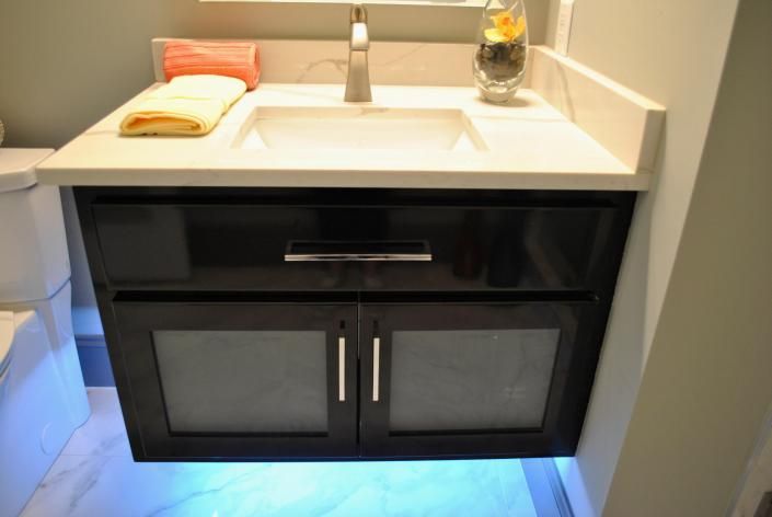 Black vanity with white countertop, sink, and faucet. Features frosted glass doors and a drawer.