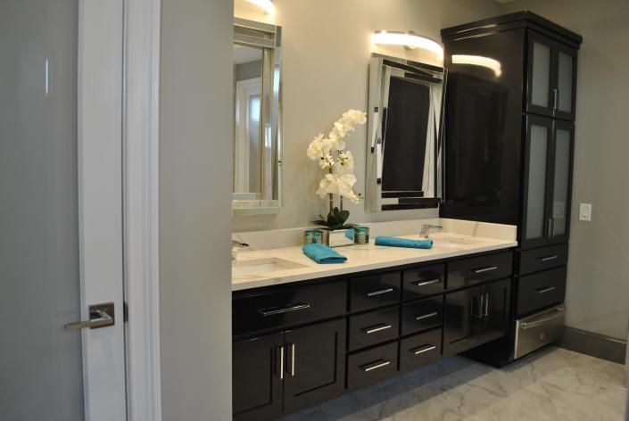 Modern bathroom with dark cabinets, dual sinks, mirrors, and a tall storage unit.