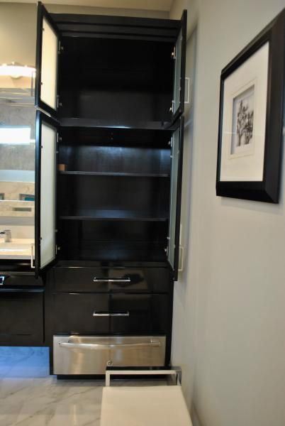 Black bathroom cabinet with open doors and a stainless steel footrest.