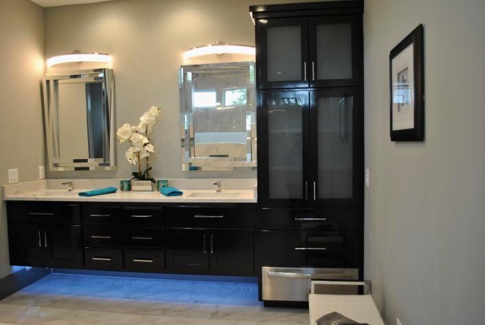 Modern bathroom with dual sinks, mirrors, black cabinets, and tall storage cabinet.